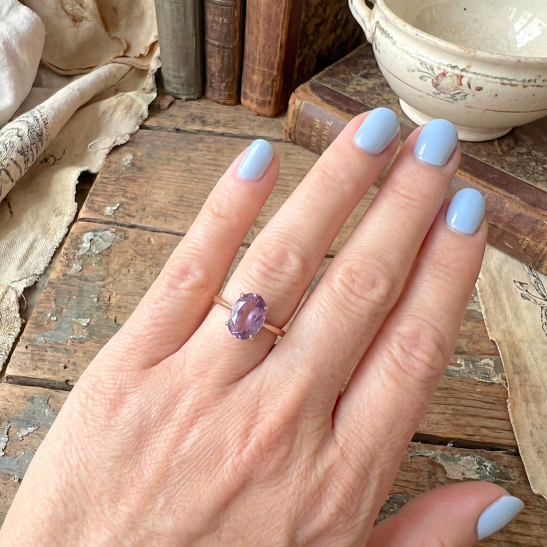 Bague solitaire avec améthyste ovale violet clair sur monture or jaune 18K, portée sur l’annulaire.
