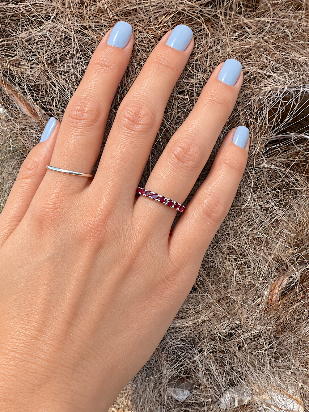 Main de femme à plat, manucure bleu clair, portant une alliance américaine rubis or gris 18K