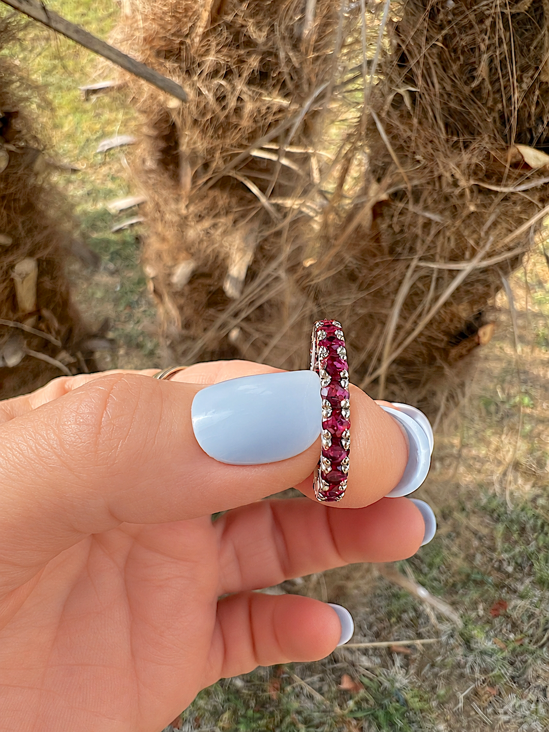 Alliance américaine rubis or gris 18K de profil, tenue entre le pouce et l'index, sertissage à 4 griffes
