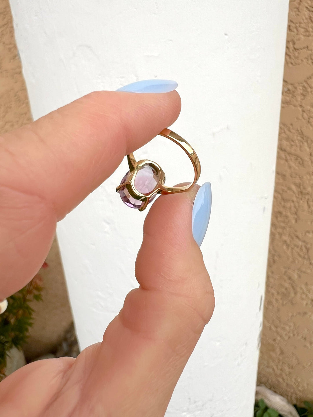 Bague améthyste ovale en or jaune 18K tenue en main sur fond blanc, vue du dessous de la monture, bijou de luxe d'occasion