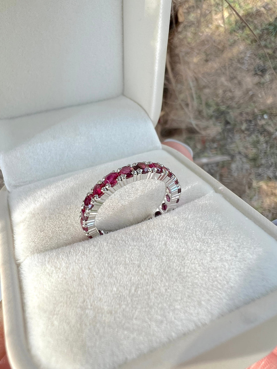 Alliance américaine en or gris 18K sertie de rubis ronds, posée dans un écrin ouvert en velours blanc
