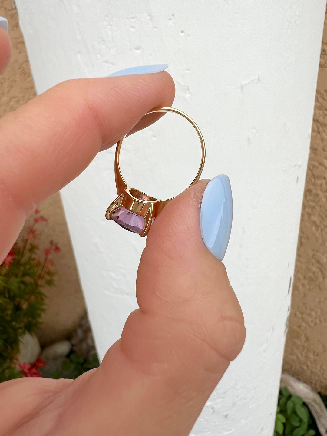 Bague femme améthyste en or jaune 18K tenue entre deux doigts sur fond blanc, anneau et monture visibles, joaillerie de luxe
