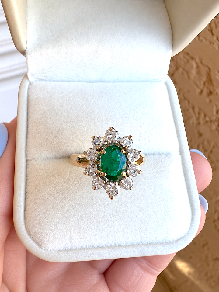 Bague marguerite émeraude et diamants or 18K dans un écrin en velours blanc, vue de face sur l'émeraude ovale entourée de 10 diamants