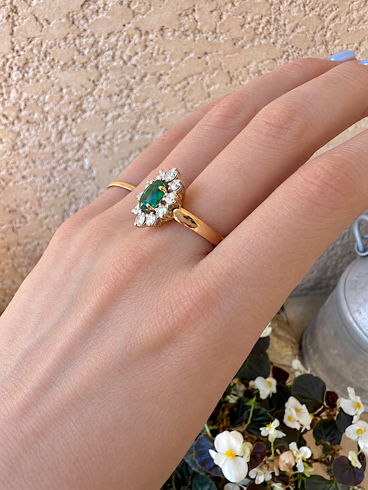 Bague marguerite émeraude et diamants or 18K portée au doigt, vue de dessus sur l'émeraude ovale, anneau fin en or jaune à côté