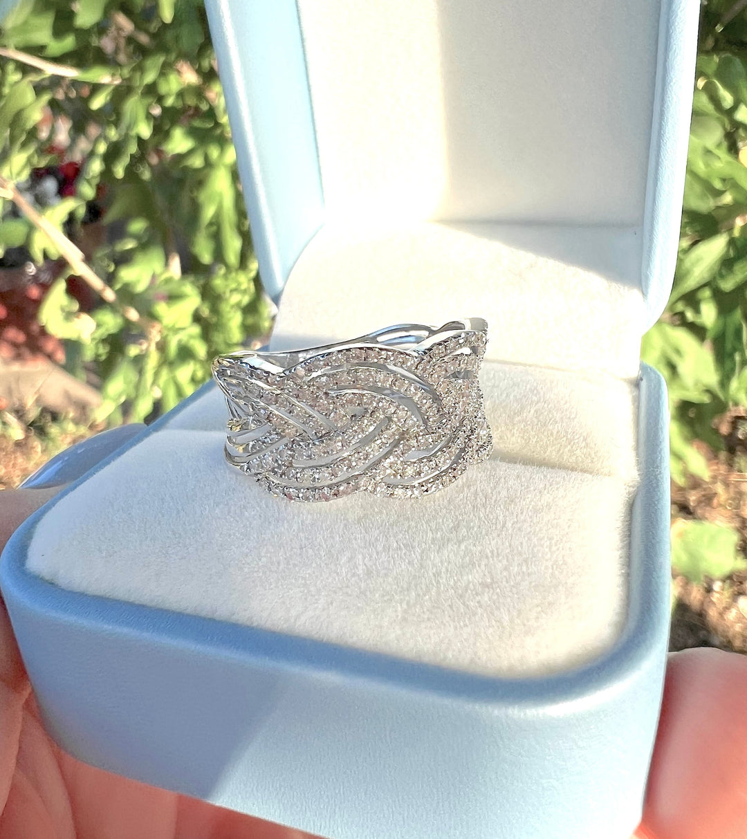 Bague diamants tressée en or blanc 18K dans un écrin bleu pastel, fond de verdure