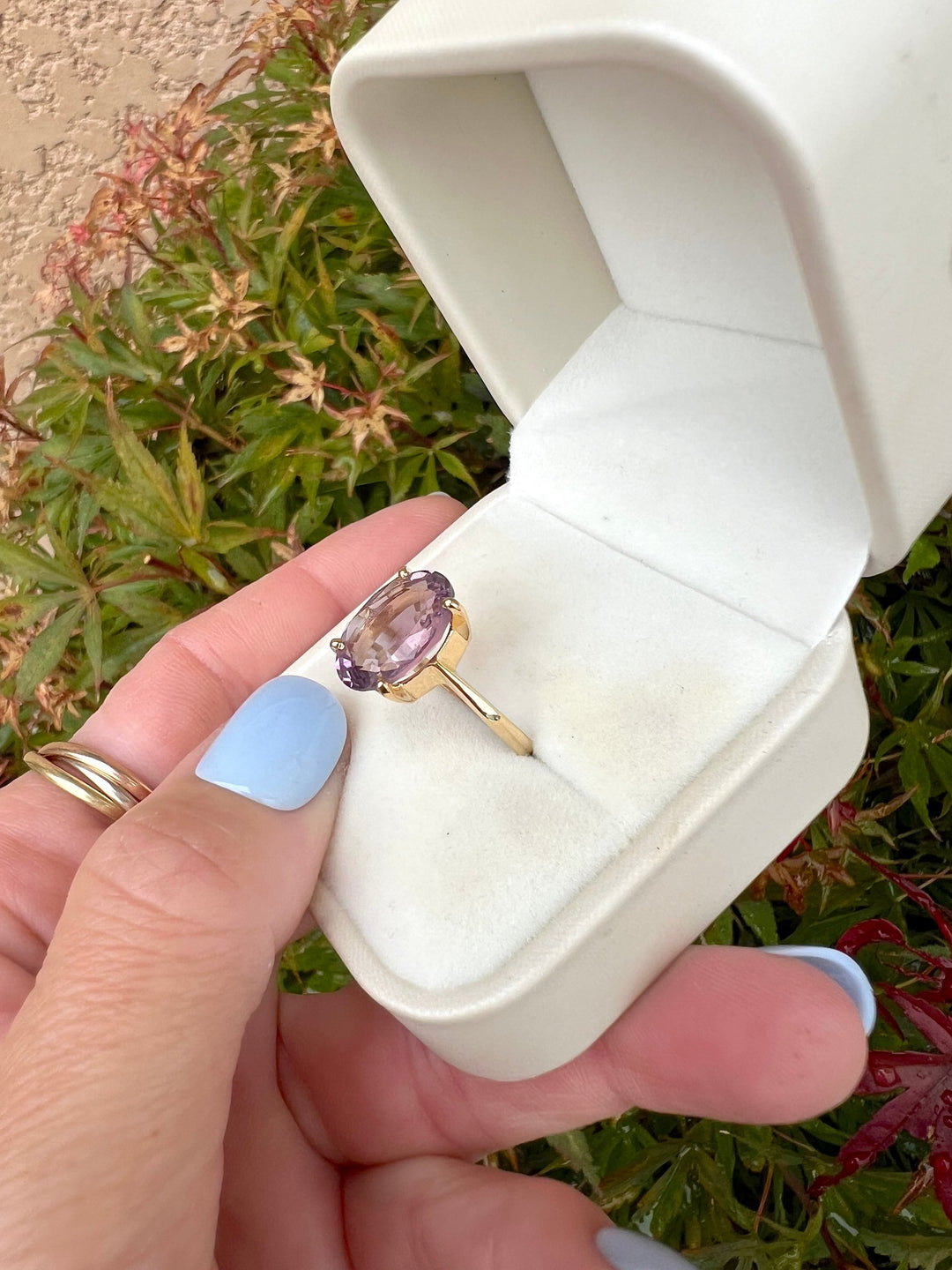 Bague joaillerie de seconde main en or jaune 18K, améthyste ovale vue de côté, écrin ouvert tenu en main