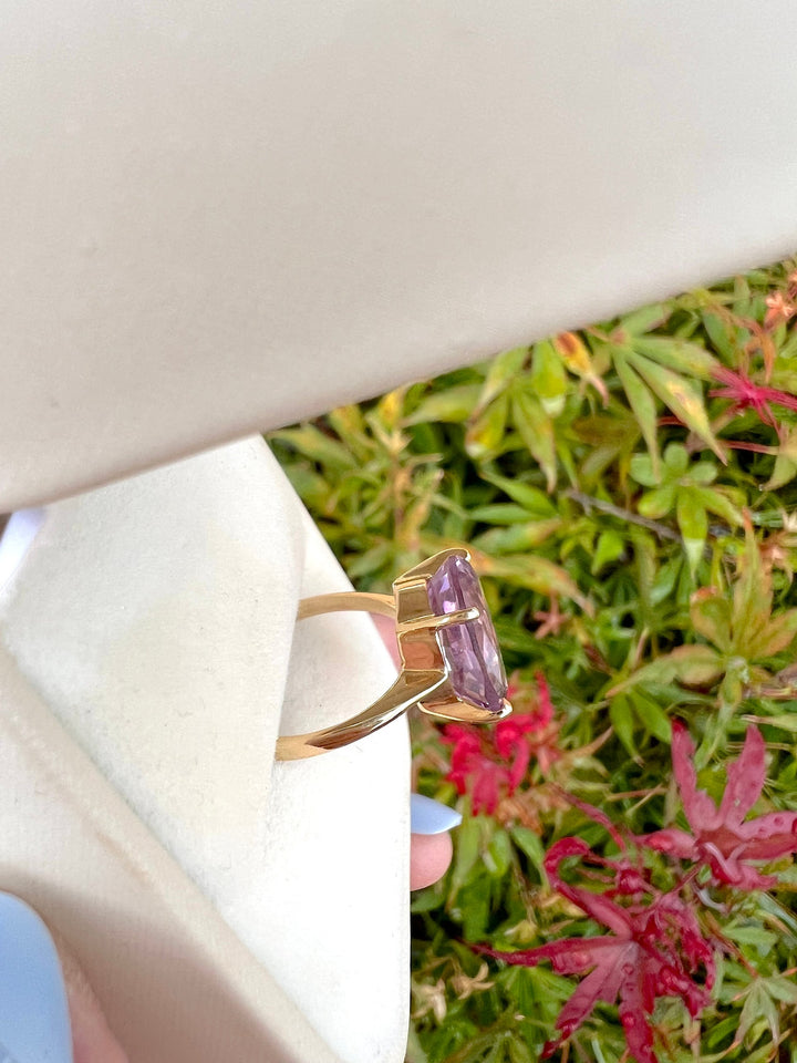 Bague améthyste ovale en or jaune 18K vue de profil, serti griffes en gros plan, tenue en main devant un érable du Japon