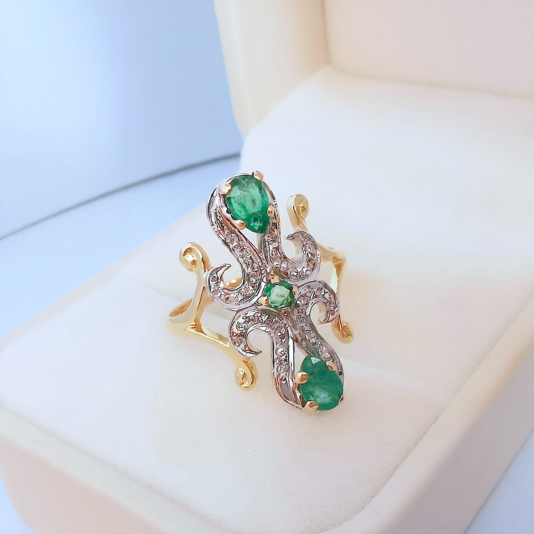 Bague marquise en or deux tons 18K sertie d'émeraudes et de diamants, présentée sur un écrin beige