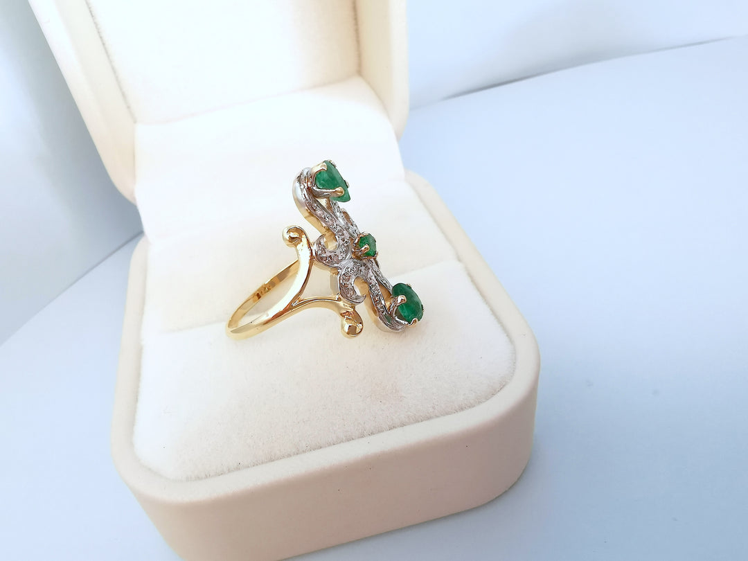 Bague marquise en or deux tons 18K avec trois émeraudes serties, posée dans un écrin
