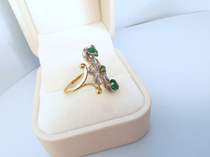 Bague marquise en or deux tons 18K avec trois émeraudes serties, posée dans un écrin