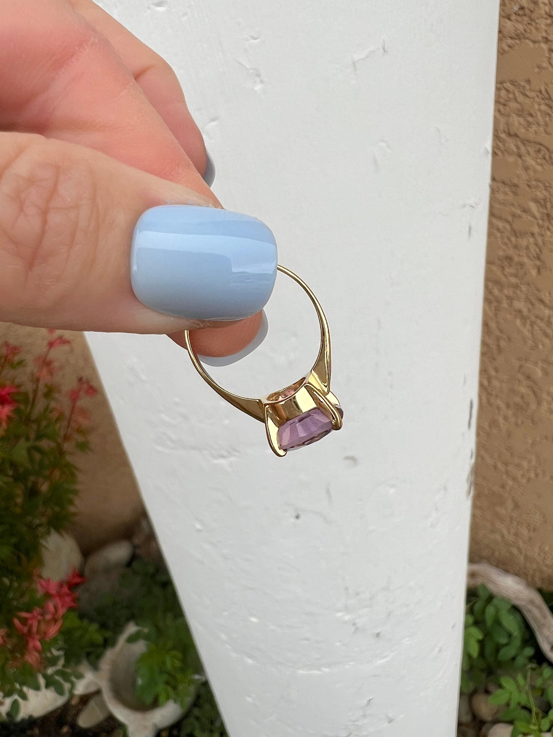 Bague solitaire or jaune et améthyste ovale tenue en main sur fond blanc, anneau et panier ajouré visibles, bijou de seconde main