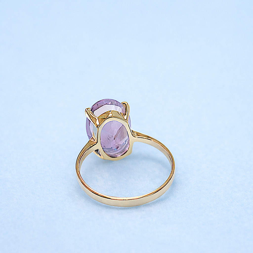 Bague en or jaune 18K avec pierre améthyste ovale en solitaire, monture griffe sur fond bleu.