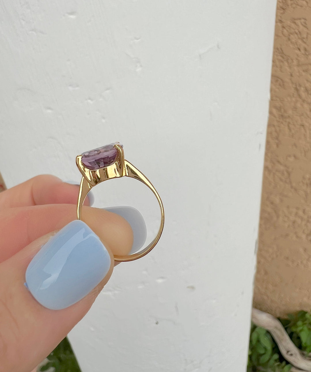Bague améthyste ovale en or jaune 18K tenue à la verticale sur fond blanc, anneau et monture vus de profil, joaillerie de luxe