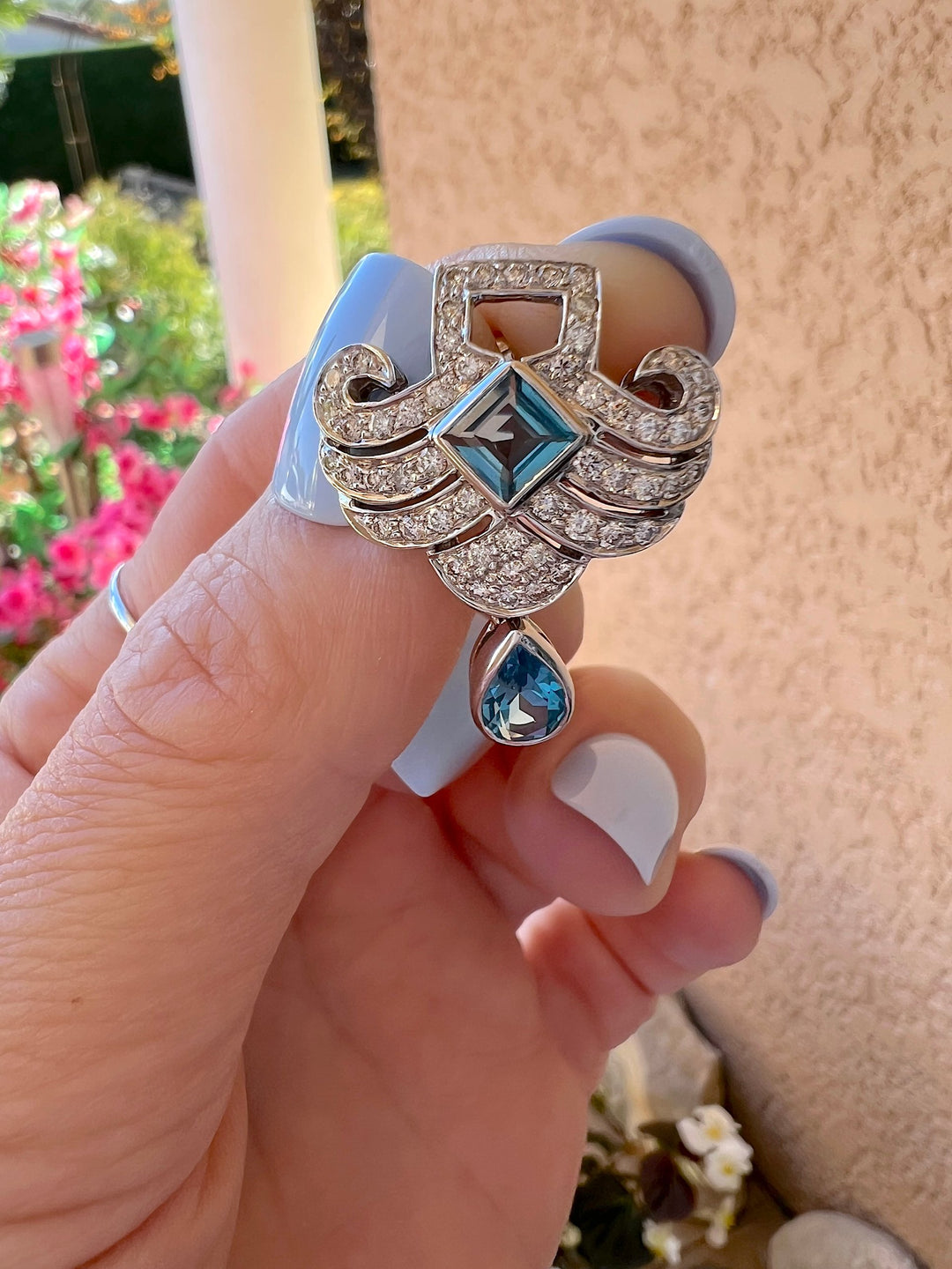 Gros plan d’une boucle d’oreille topaze bleue taille émeraude et diamants en or gris 18K, tenue entre les doigts