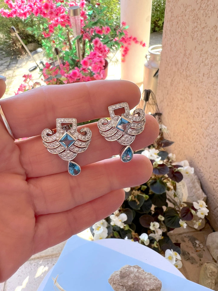 Paire de boucles d’oreilles topazes bleues et diamants en or gris 18K tenue dans la main, jardin fleuri