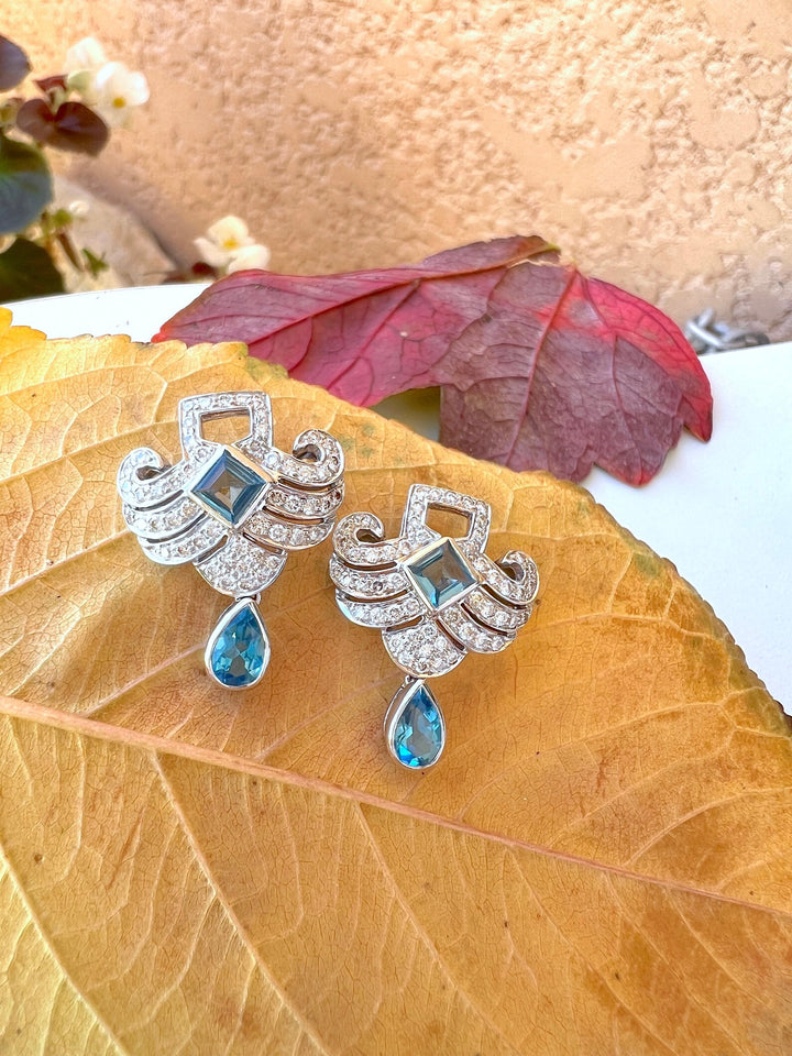 Boucles d’oreilles topazes bleues et diamants en or gris 18K posées sur une feuille d’automne dorée