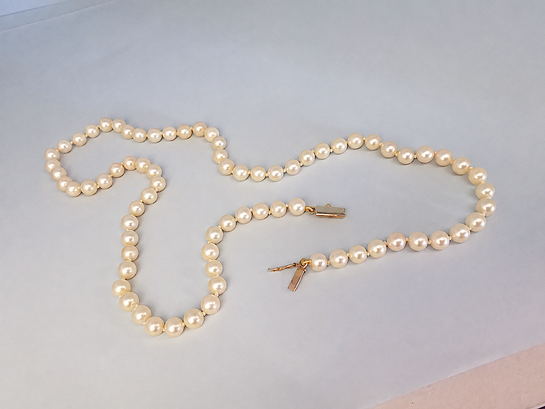 Collier de perles de culture posé à plat sur fond blanc, fermoir en or jaune 18K ouvert, détail de la joaillerie