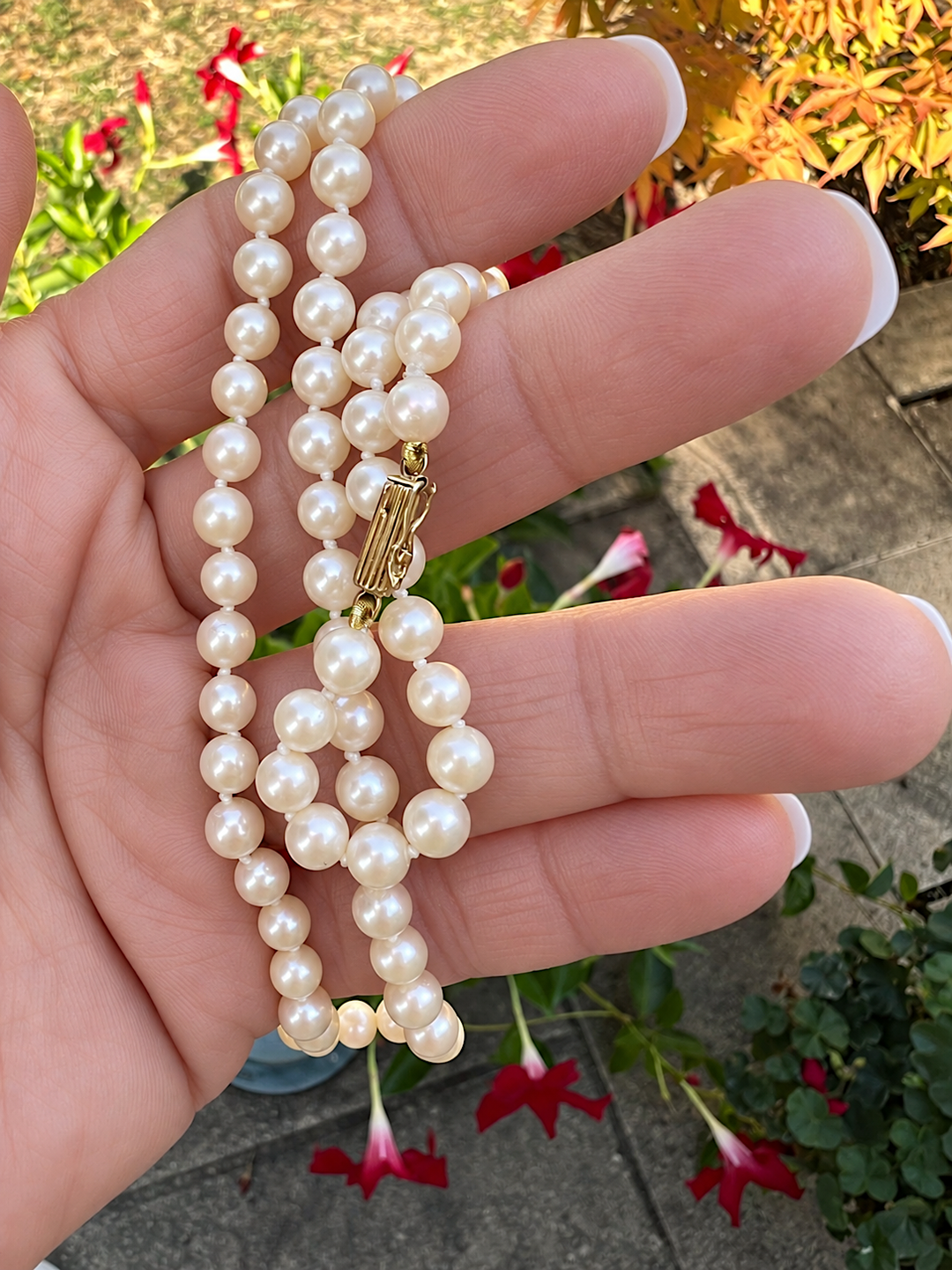 Collier de perles tenu dans la paume, fermoir en or jaune 18K au centre, joaillerie pour femme en extérieur