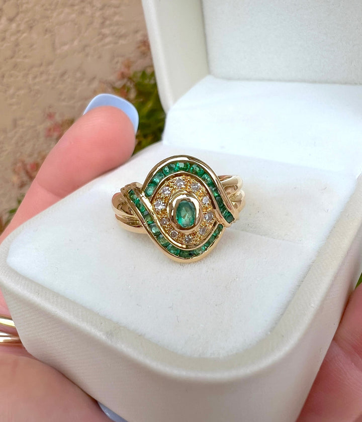 Gros plan macro d'une bague émeraudes et diamants en or jaune 18K, joaillerie de seconde main, en écrin blanc