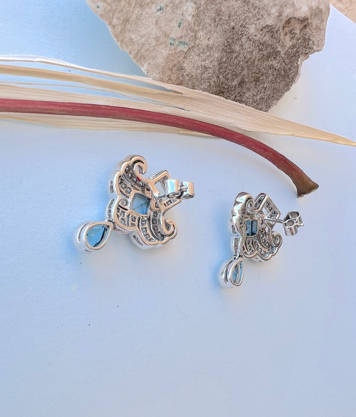 Dos des boucles d’oreilles en or gris 18K, topazes bleues et diamants, sur fond bleu avec tige rouge