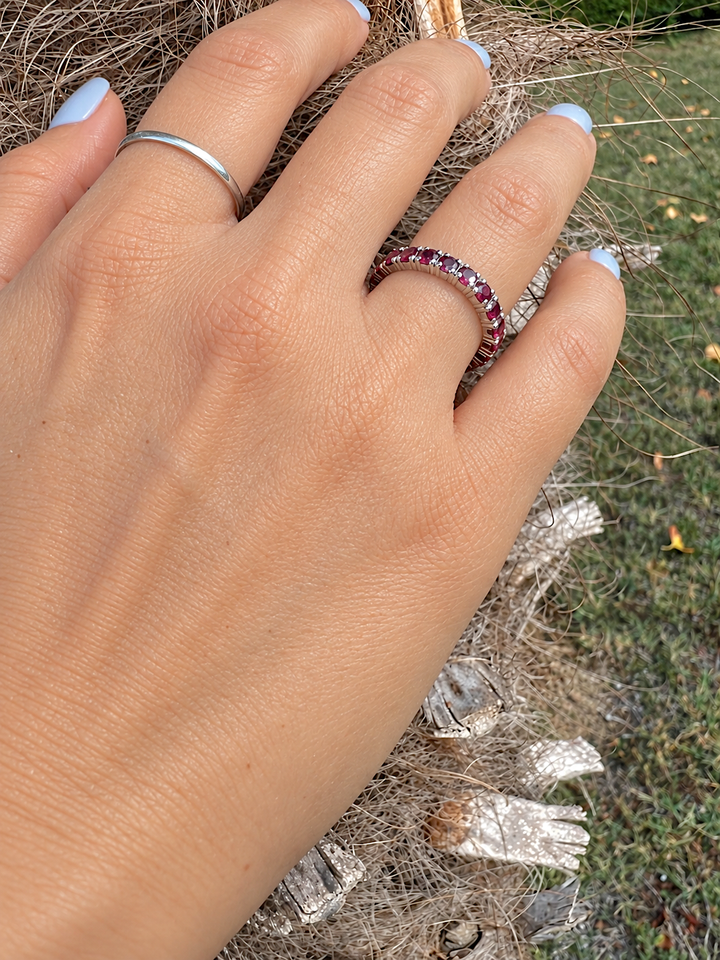 Alliance américaine de rubis en or gris 18K portée, dos de la main, vue de biais sur fond de palmier