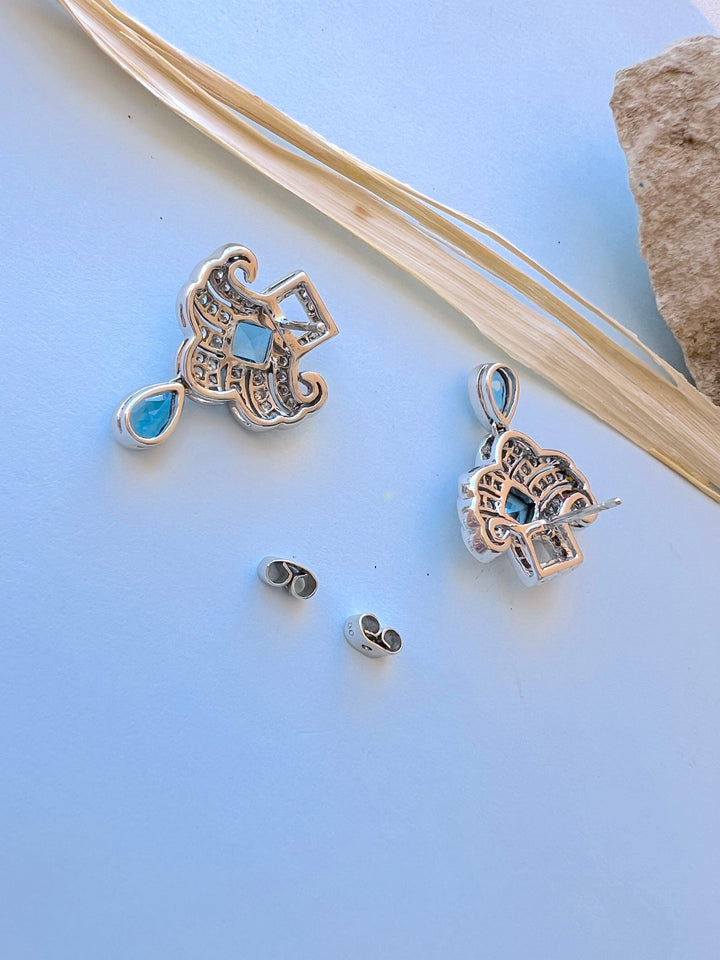 Boucles d’oreilles or gris 18K et topazes bleues vues de dos avec leurs fermoirs papillon sur fond bleu