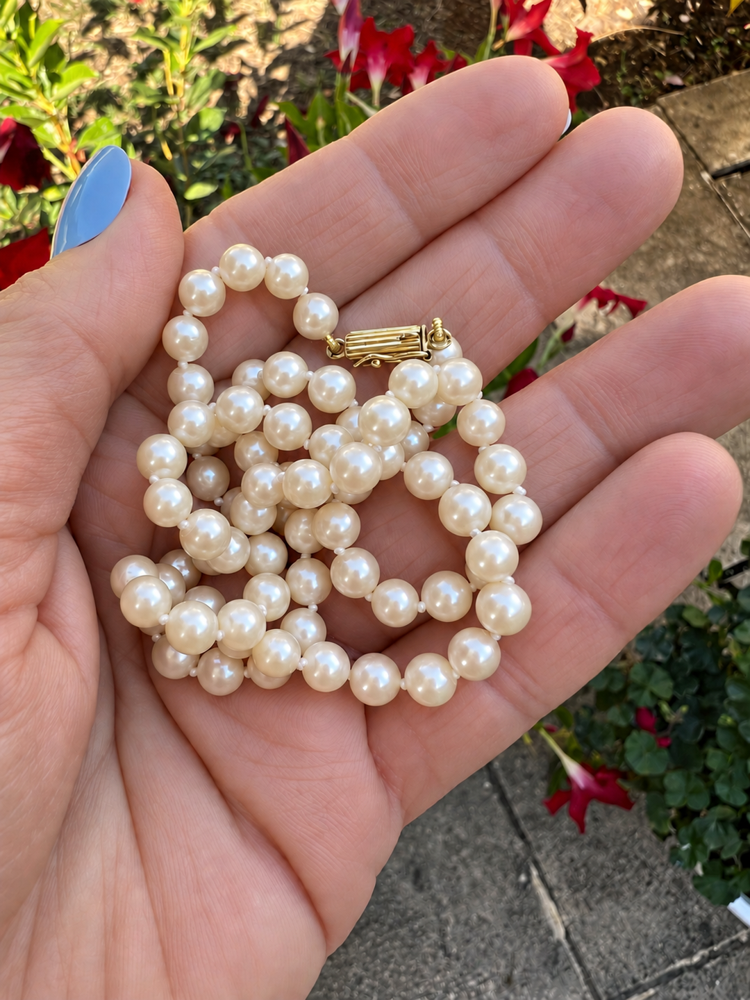 Collier de perles de culture enroulé dans la paume de la main, fermoir en or visible, joaillerie de seconde main