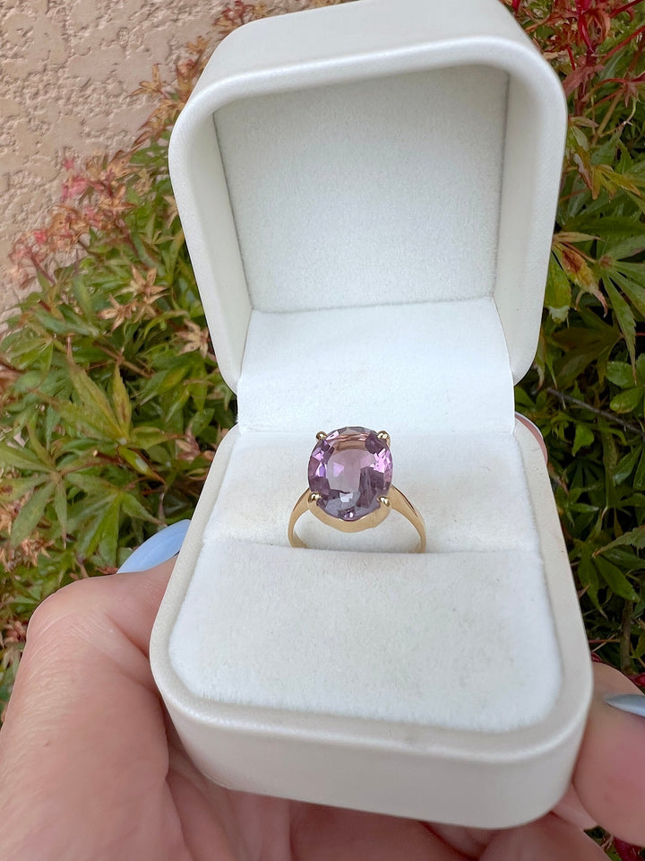 Bague solitaire améthyste ovale en or jaune 18K dans un écrin ouvert crème, pierre vue de face, joaillerie pour femme